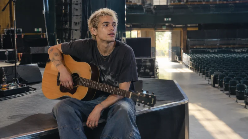 Dominic Fike with an acoustic guitar backstage